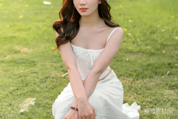 高清摄影 一位穿着白色连衣裙的女人坐在草地上。