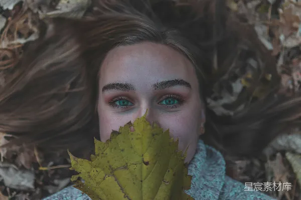 高清摄影 女人躺在干枯的树叶上，手里拿着一片绿叶。