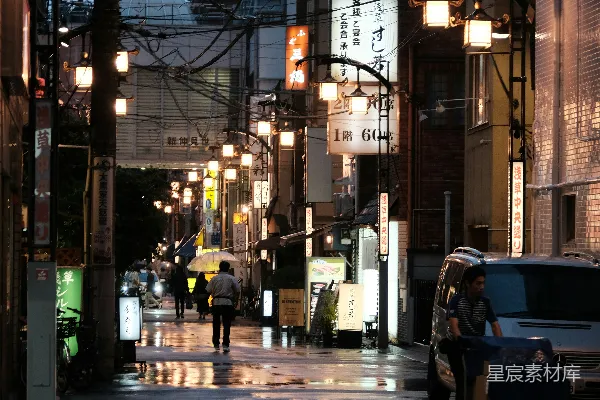 高清摄影 一条湿漉漉的夜晚城市街道，人们在人行道上行走。