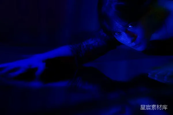 高清摄影 一个女人在昏暗的房间里，房间内有蓝色的灯光。