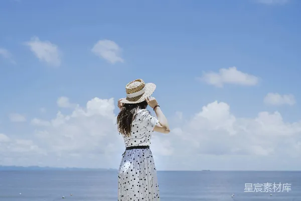 高清摄影 一个穿着连衣裙并戴着帽子的人站在一片水域前。