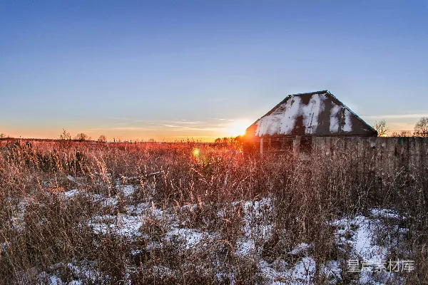 高清摄影 夕阳照耀在积雪覆盖的田野上，旁边有一座谷仓。