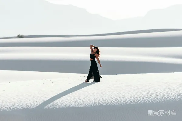 高清摄影 穿着黑色连衣裙的女人在白天的白色沙滩上行走。
