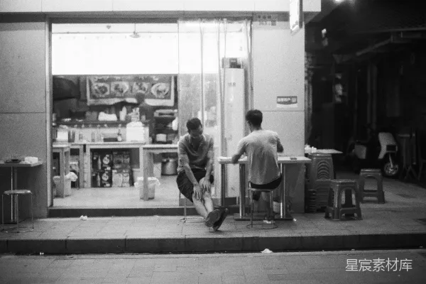 高清摄影 两个人在商店外面的桌子旁坐着，夜晚时分。