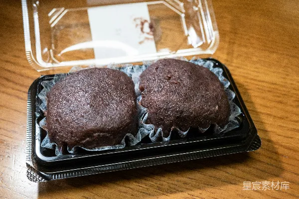 高清摄影 两个巧克力松饼放在塑料容器中，放在木桌上。