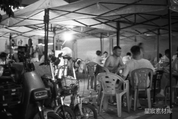 高清摄影 人们在帐篷下用餐，附近停放着电动车。