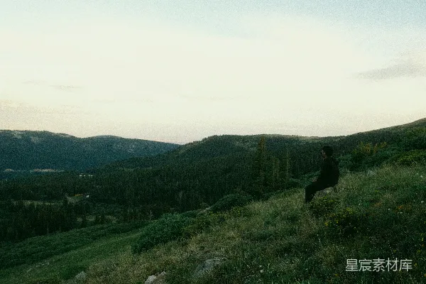 高清摄影 一个男人坐在草地上，俯瞰着黄昏时分的群山。