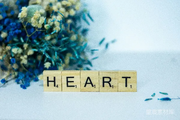 高清摄影 一个木制的方块，上面拼写着单词“heart”，旁边是一束花。