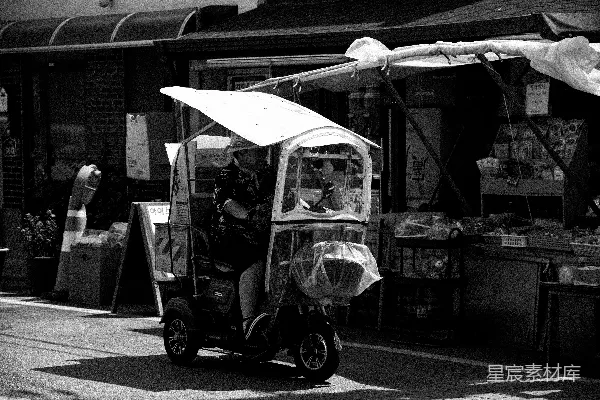 高清摄影 一个人骑着一辆带顶棚的滑板车在街上。