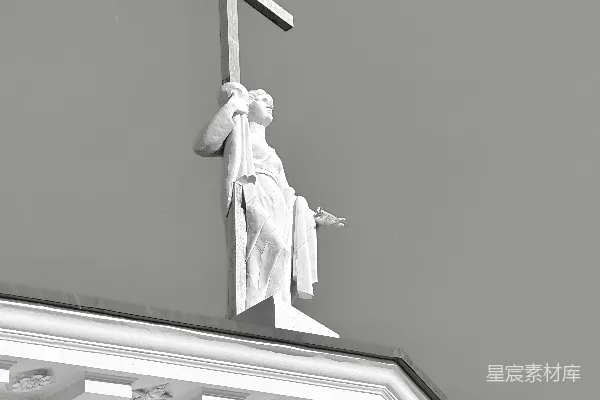 高清摄影 一座雕像高举着十字架，矗立在一座建筑的顶端。