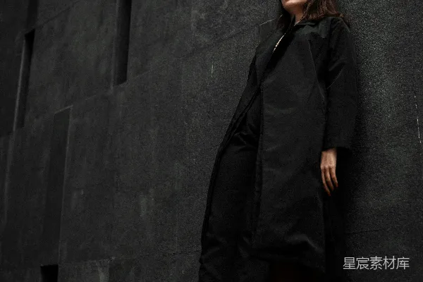 高清摄影 一个靠在墙边的女人，穿着一件黑色外套。