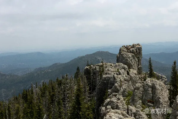 高清摄影 一块岩石露出地面，周围有树木，远处是山脉。
