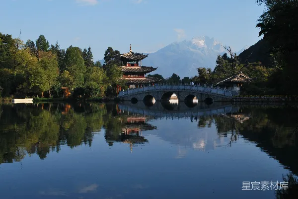 高清摄影 白天，河上有一座棕色和黑色相间的桥，桥的周围是茂密的绿色树木，天空湛蓝。