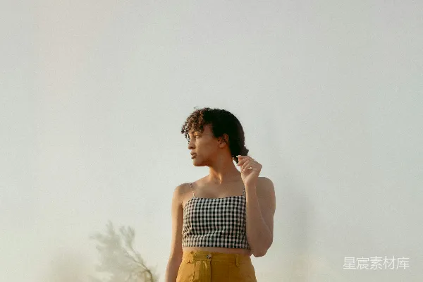 高清摄影 穿着黑白条纹背心和棕色裤子的女人站在白色墙边。