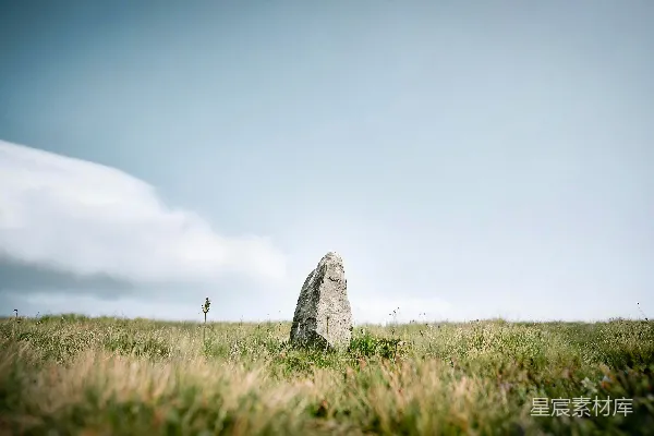 高清摄影 一块石头矗立在草地上，天空多云。