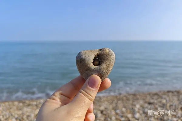 高清摄影 拿着一颗心形的石头，海景在后面。