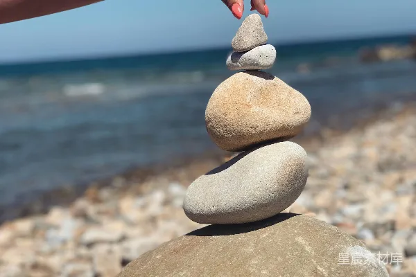 高清摄影 一个人在海滩上堆叠石头，背景是海洋。