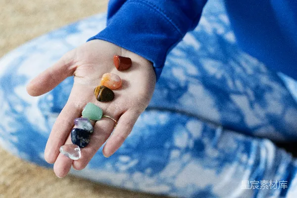 高清摄影 一只手拿着彩色的充满活力的气场治疗宝石，放在垫子上。