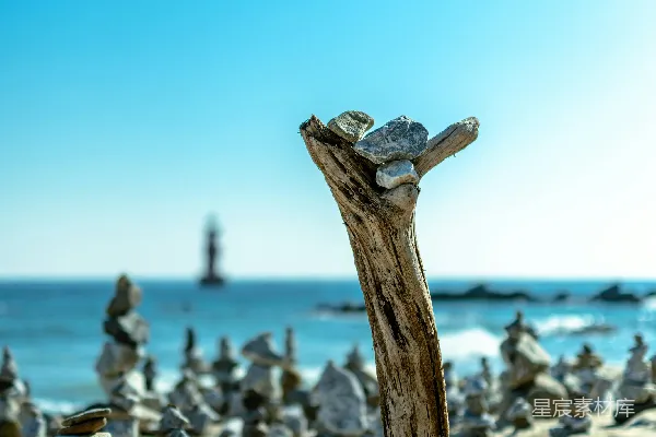 高清摄影 阳光明媚的海滩上有漂流木和平衡的石头。