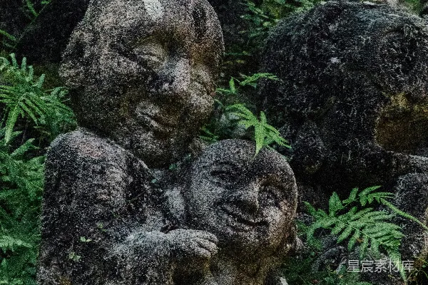 高清摄影 被苔藓覆盖的石雕，上面雕刻着笑脸儿童在绿叶中。