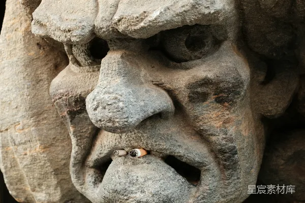 高清摄影 石雕一个丑陋的、愤怒的脸孔，手里拿着一支烟。