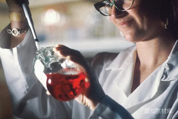 高清摄影 穿着实验服的女人拿着一个装有液体的烧瓶