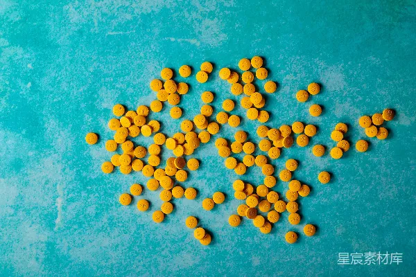 高清摄影 一堆黄色药片放在蓝色表面上。