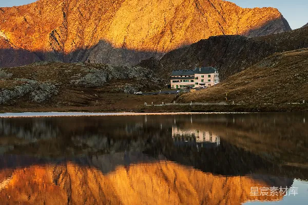高清摄影 一座湖边的小山上的房子，背景中有一座山。
