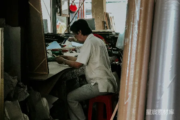 高清摄影 坐在红色塑料凳子上的男人正在使用手机，旁边有一张桌子。