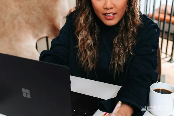 高清摄影 穿黑色毛衣的女人坐在桌子旁，桌上有一台黑色的微软Surface笔记本电脑。