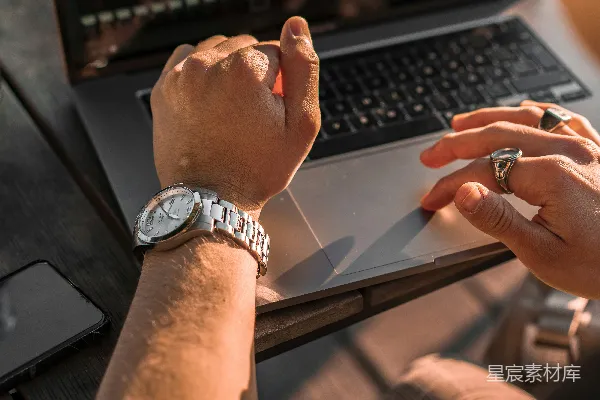 高清摄影 佩戴银色链条手镯和圆形模拟手表的人使用MacBook Pro电脑。