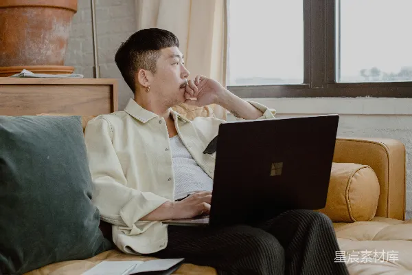 高清摄影 穿着白色衬衫和黑色裤子的男人坐在沙发上，使用Surface笔记本电脑。