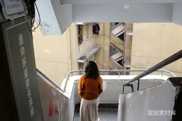 高清摄影 穿着橙色毛衣的女人正低头看向楼梯间。