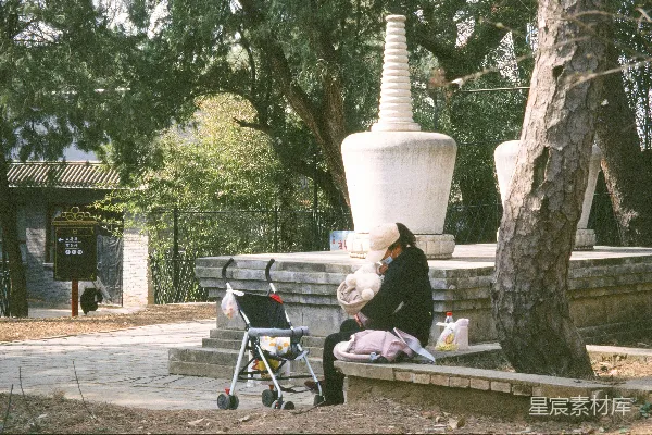 高清摄影 一位妇女坐在凳子旁边，靠近一辆婴儿车。