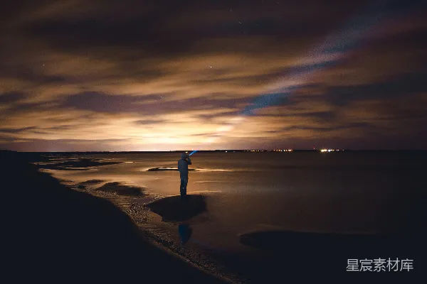 高清摄影 海滩上的夜景：手电筒照亮的孤独身影