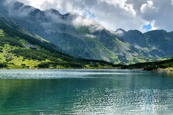 高清摄影 绿色和灰色的山峦位于水体旁边，在蓝天白云的背景下在白天出现