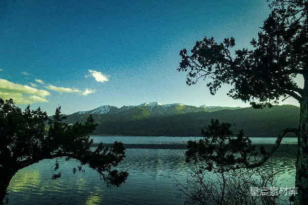 高清摄影 一片被树木和山脉环绕的湖泊，在蓝天之下。