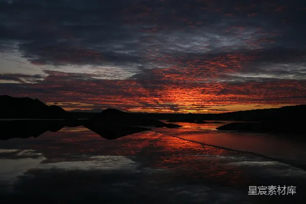 高清摄影 夕阳映照在一片水体上，山峦在背景中若隐若现。
