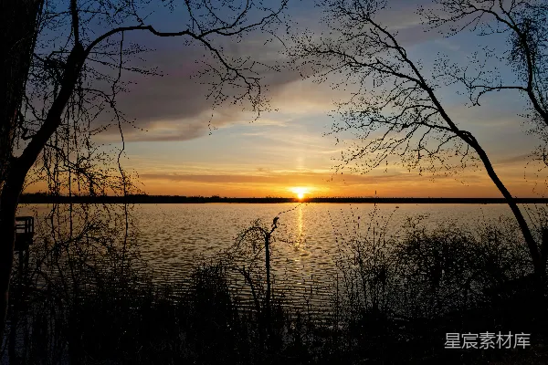高清摄影 夕阳映照着平静的湖面，树影倒映其中。